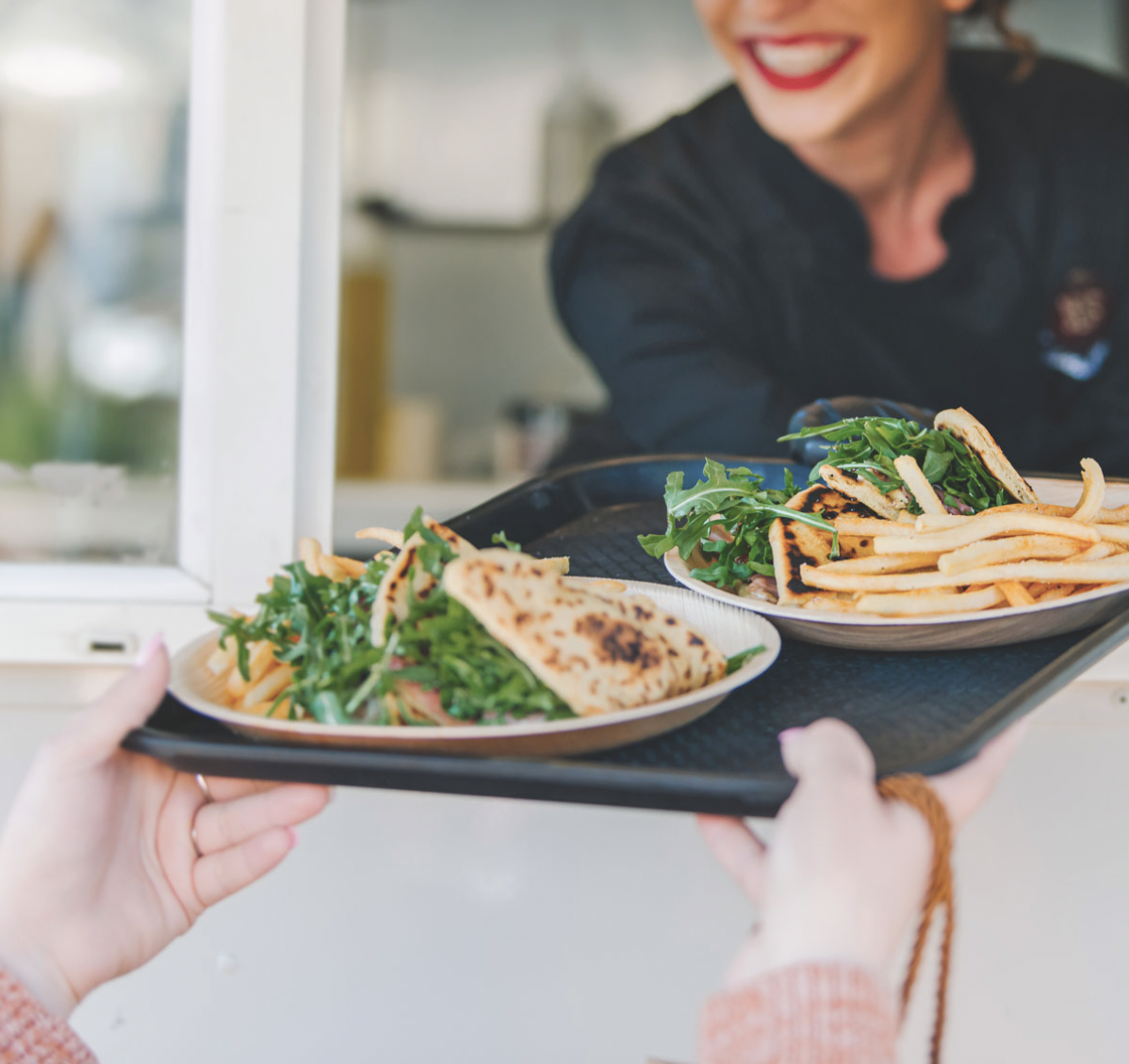 Food truck attendant handing over two plates of flatbread and fries