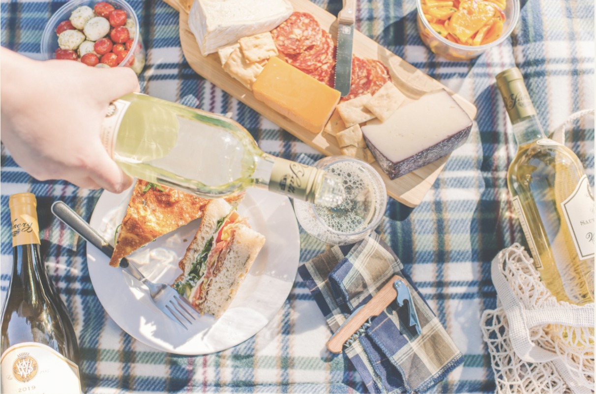 Picnic blanket spread with wine, cheese board and sandwiches
